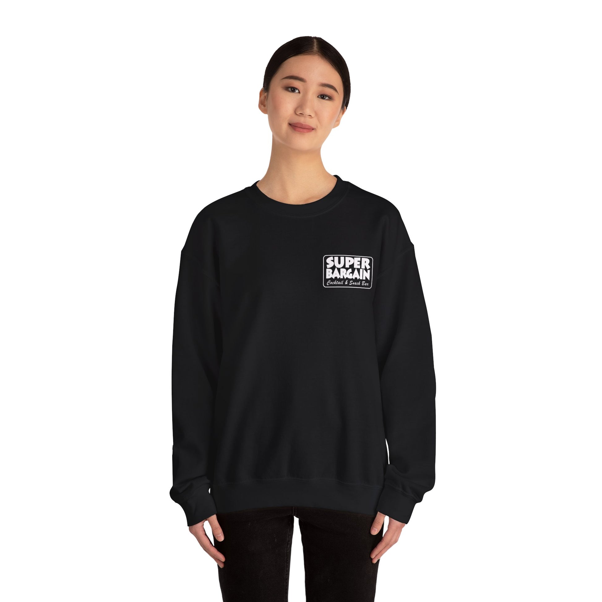 A young Asian woman stands in Cabbagetown, Toronto, wearing a black Printify Unisex Heavy Blend™ Crewneck Monochrome Logo and Cabbagetown sweatshirt with the text "SUPER BARGAIN" printed in white and red on the chest. She has a neutral expression and her hands are by her sides.