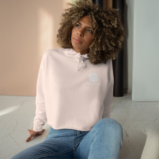A woman with curly hair wearing a Printify Crop Hoodie with Monochrome Cabbagetown and Super Bargain Logo and jeans sits on the floor, gazing thoughtfully to her side in a room with sunlight streaming in, in Toronto’s Cabbagetown.