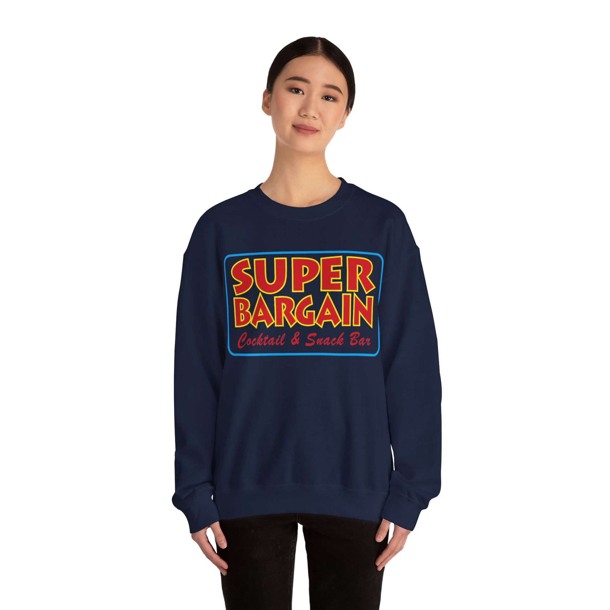 A young Asian woman wearing a Printify's Unisex Heavy Blend™ Crewneck Signature Logo Sweatshirt in dark blue with the words "SUPER BARGAIN Cocktail & Snack Bar" in colorful bold font stands confidently against a white background, in Toronto's Cabbagetown neighborhood.