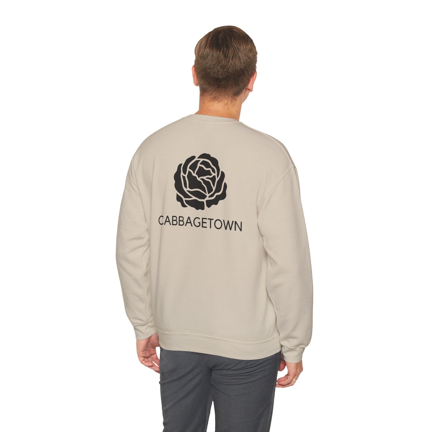 Man viewed from the back wearing a beige Unisex Heavy Blend™ Crewneck Monochrome Logo and Cabbagetown Sweatshirt with a black "Toronto Cabbagetown" logo and a stylized cabbage graphic above the text by Printify.