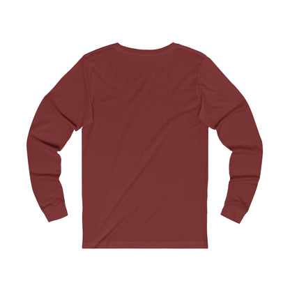 A plain maroon Unisex Jersey Long Sleeve Signature Logo Tee displayed on a flat white surface with a view of the back. The fabric appears smooth and the garment is laid out to maintain its shape, reminiscent of styles seen in Toronto's Cabbagetown. (Printify)
