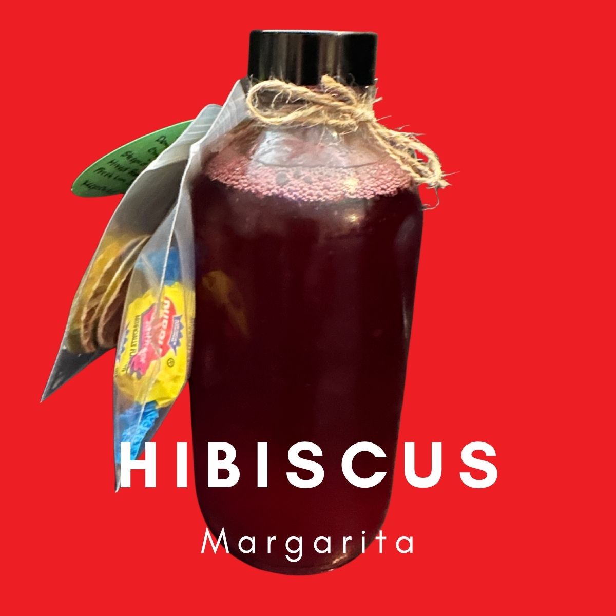 A bottle of Hibiscus Berry Margarita RTD Cocktail mix against a red background, labeled with "HIBISCUS Margarita". The bottle has a burlap tie and a decorative leaf attached.