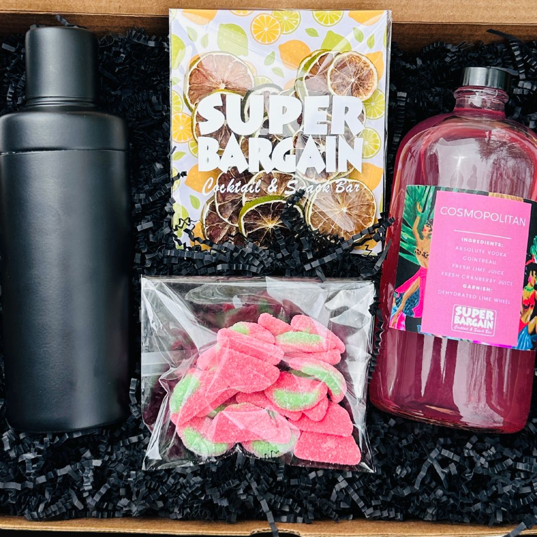 A large ready-to-drink cosmopolitan gift box featuring a stylish design, containing 1 large bottles of 8 pre-mixed cosmopolitan cocktails and accompanying garnishes, a sweet or savory treat and a matte cocktail shaker.