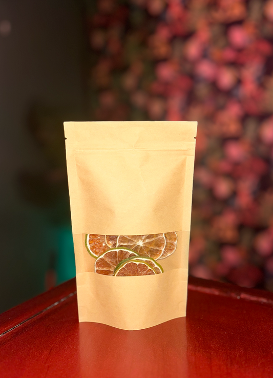 A brown paper bag with a transparent window revealing Super Bargain Shop dehydrated lime wheel garnishes, placed on a shiny red surface against a blurred backdrop.