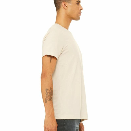 Side profile of a person wearing the Super Bargain "I Like My Whiskey Neat" tee in a soft, light beige color and unisex sizing, paired with dark jeans. The individual's right arm features a distinctive tattoo design. They stand against a white background, showcasing the stylish Super Bargain apparel.